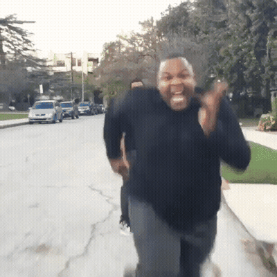 A Man In A Black Sweater Is Running Down A Street And Making A Funny Face GIF