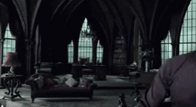 A Man In A Black Sweater Is Sitting In A Living Room With A Couch And A Lamp . GIF