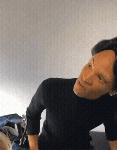 A Man In A Black Sweater Is Sitting On A Bed And Looking At Something GIF