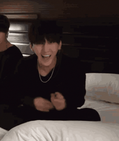 A Man In A Black Sweater Is Sitting On A Bed GIF