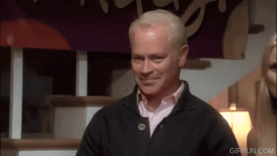 A Man In A Black Sweater Is Smiling In Front Of A Sign That Says " Gifrun.com " GIF