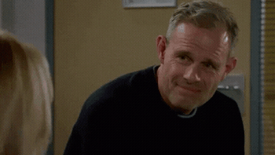 A Man In A Black Sweater Is Smiling While Looking At A Woman GIF