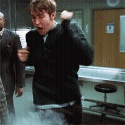 A Man In A Black Sweater Is Standing In A Room With A Sign On The Wall That Says No Smoking GIF