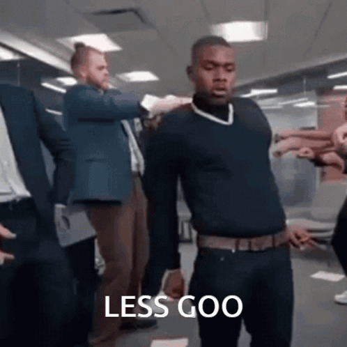 A Man In A Black Sweater Is Standing In Front Of A Group Of People With The Words Less Goo Written On The Bottom . GIF