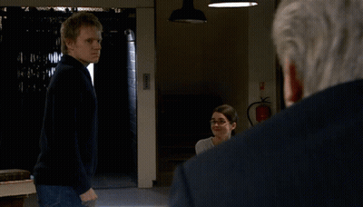 A Man In A Black Sweater Stands In Front Of A Fire Extinguisher In A Dark Room GIF