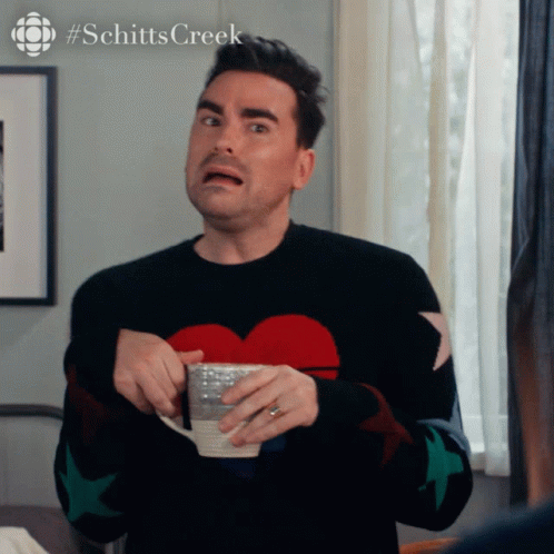 A Man In A Black Sweater With A Heart On It Is Holding A Cup Of Coffee GIF