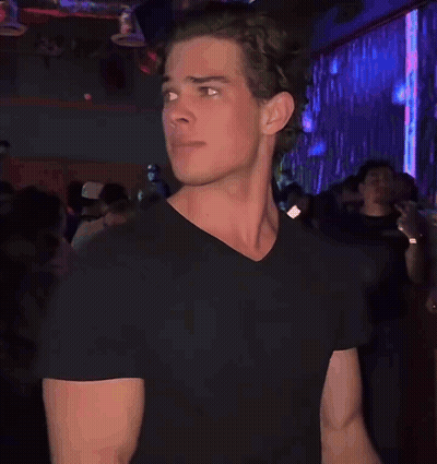 A Man In A Black T-Shirt Is Standing In A Crowded Room GIF