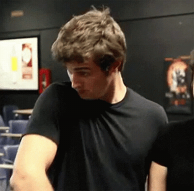 A Man In A Black T-Shirt Is Standing In A Dark Room . GIF
