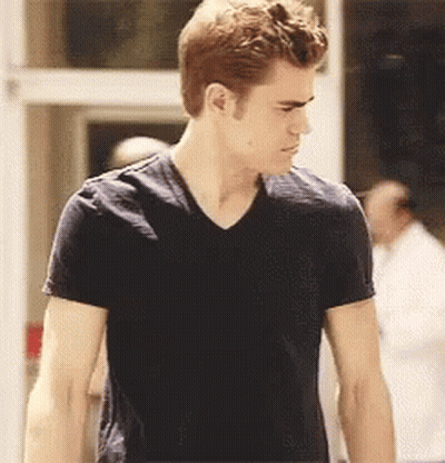 A Man In A Black T-Shirt Is Standing In Front Of A Door GIF