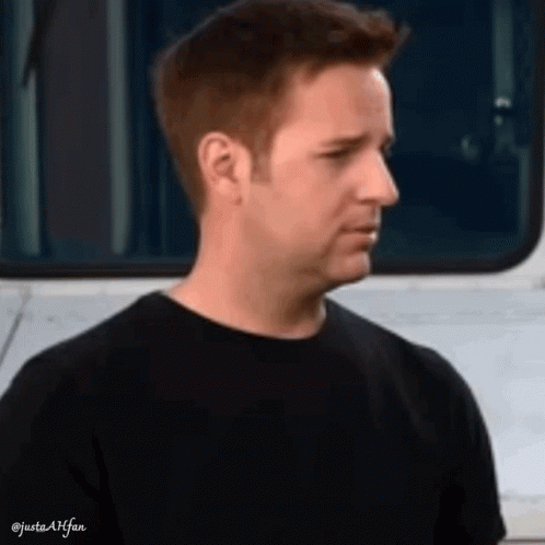 A Man In A Black T-Shirt Is Standing In Front Of A White Van . GIF