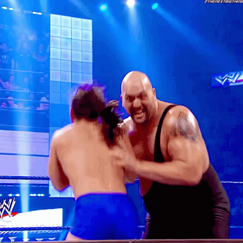 A Man In A Black Tank Top Is Fighting Another Man In Blue Shorts In A Wrestling Ring GIF