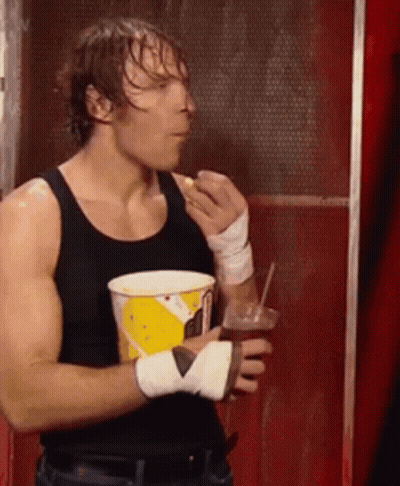 A Man In A Black Tank Top Is Holding A Cup Of Popcorn And A Drink . GIF