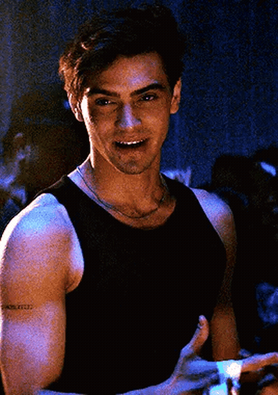 A Man In A Black Tank Top Is Smiling And Holding A Remote Control In His Hand . GIF