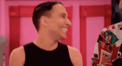 A Man In A Black Tank Top Is Smiling And Laughing While Standing Next To Another Man In A Colorful Shirt . GIF