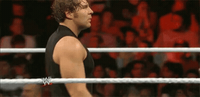 A Man In A Black Tank Top Is Standing In A Wrestling Ring With A Crowd Watching . GIF