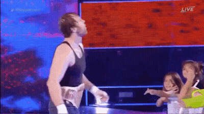 A Man In A Black Tank Top Is Standing In A Wrestling Ring With A Group Of Children . GIF