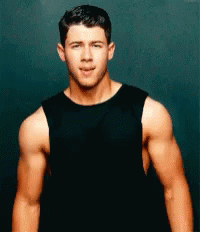 A Man In A Black Tank Top Is Standing In Front Of A Black Wall . GIF