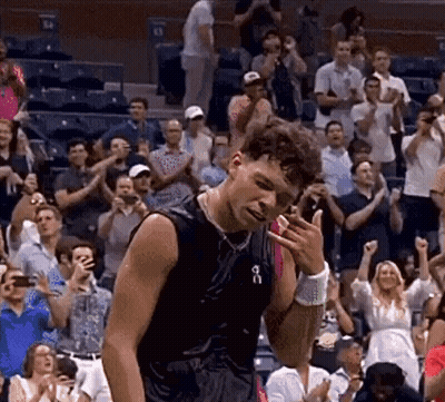 A Man In A Black Tank Top Is Standing In Front Of A Crowd Of People Applauding . GIF