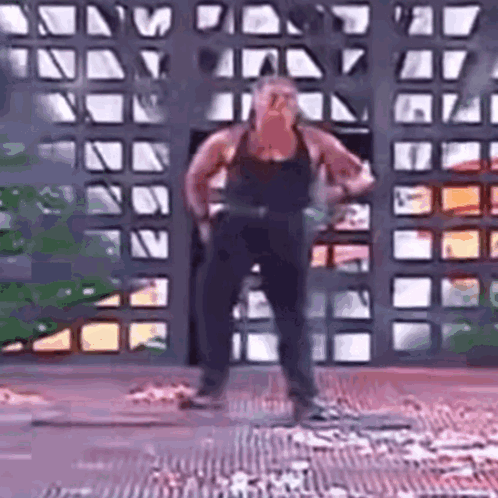 A Man In A Black Tank Top Is Standing In Front Of A Fence . GIF