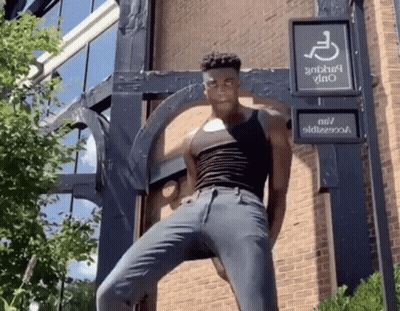 A Man In A Black Tank Top Is Standing In Front Of A Handicap Sign GIF