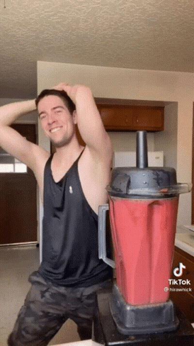 A Man In A Black Tank Top Is Standing Next To A Red Blender GIF