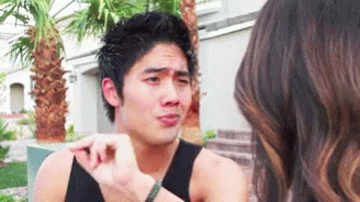 A Man In A Black Tank Top Is Talking To A Woman With Palm Trees In The Background GIF