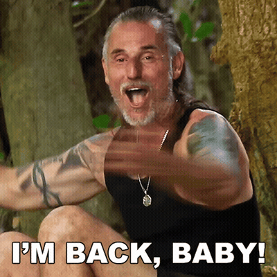 A Man In A Black Tank Top Says I 'M Back Baby While Sitting In The Woods GIF