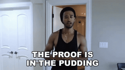 A Man In A Black Tank Top Stands In Front Of A Door With The Words The Proof Is In The Pudding Above Him GIF