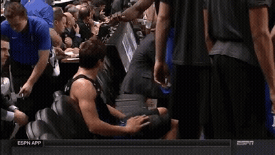 A Man In A Black Tank Top With The Number 1 On It Is Sitting On The Floor GIF