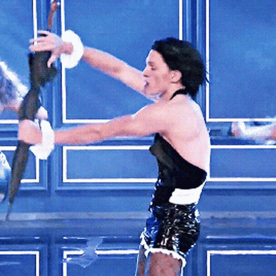 A Man In A Black Top And Shorts Is Holding A Stick GIF