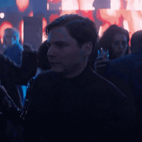 A Man In A Black Turtleneck Stands In A Crowd GIF