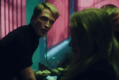 A Man In A Black Turtleneck Talks To A Woman In A Dark Room GIF