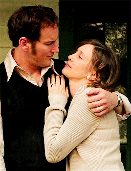A Man In A Black Vest Is Hugging A Woman In A White Sweater GIF
