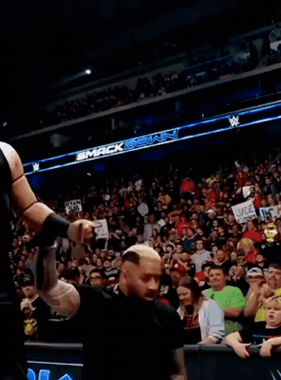 A Man In A Black Vest Is Standing In Front Of A Crowd In A Stadium . GIF