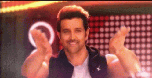 A Man In A Black Vest With A Cross On It Is Smiling And Giving A Peace Sign . GIF