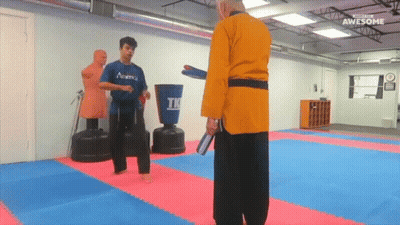 A Man In A Blue Academy Shirt Is Kicking A Man In A Yellow Robe GIF