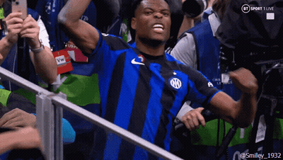 A Man In A Blue And Black Striped Shirt Stands In Front Of A Bt Sport 1 Live Camera GIF