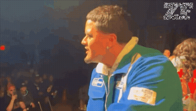 A Man In A Blue And Green Jacket Stands In Front Of A Crowd With The Number 20 On The Bottom GIF