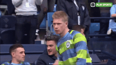 A Man In A Blue And Green Striped Shirt Stands In A Stadium With A Play Sports Logo Behind Him GIF