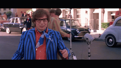 A Man In A Blue And Red Striped Suit And Tie Stands On A Street GIF