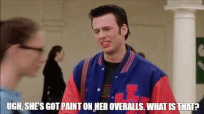A Man In A Blue And Red Varsity Jacket Is Talking To A Woman In A Hallway . GIF