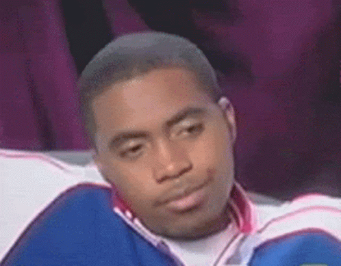 A Man In A Blue And White Jacket Is Sitting On A Couch Making A Funny Face . GIF