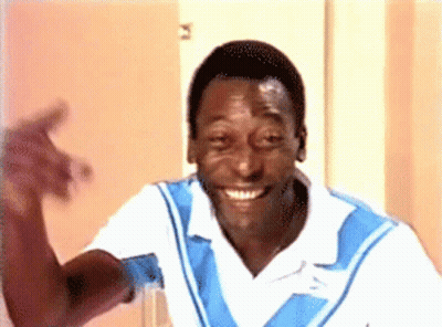 A Man In A Blue And White Shirt Is Smiling And Waving His Hand GIF
