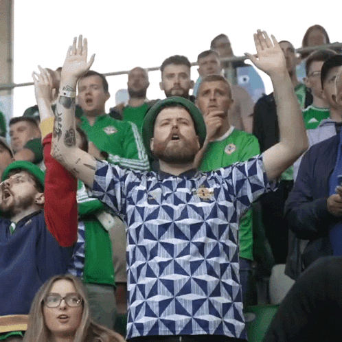 A Man In A Blue And White Shirt Stands In A Crowd GIF