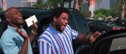 A Man In A Blue And White Striped Shirt Is Laughing With Another Man In A Car GIF