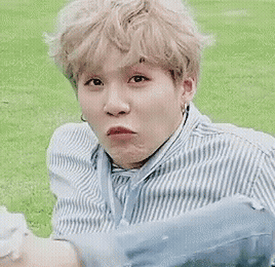A Man In A Blue And White Striped Shirt Is Sitting In The Grass With A Dog . GIF