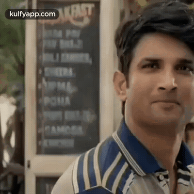 A Man In A Blue And White Striped Shirt Is Standing In Front Of A Restaurant . GIF