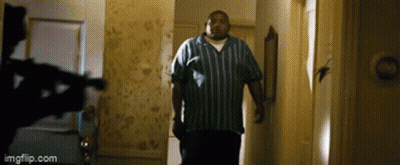 A Man In A Blue And White Striped Shirt Is Walking Down A Hallway . GIF