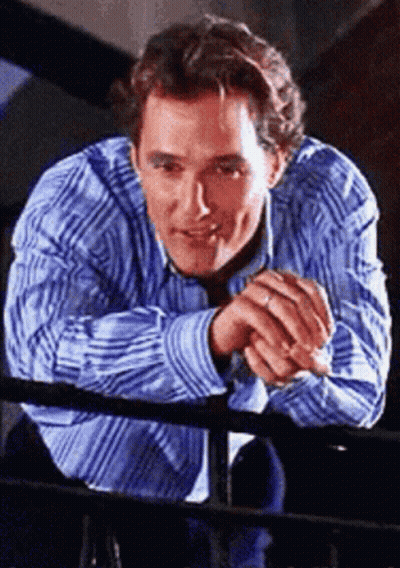 A Man In A Blue And White Striped Shirt Leans On A Railing GIF