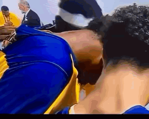 A Man In A Blue And Yellow Shirt Is Kissing Another Man On The Cheek . GIF